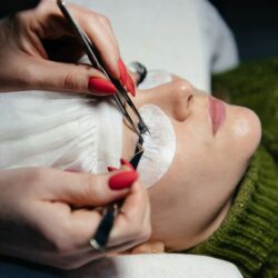 eyelash extension process closeup portrait young girl woman with long thick eyelashes eyes closed hand cosmetologist adding more eyelashes her